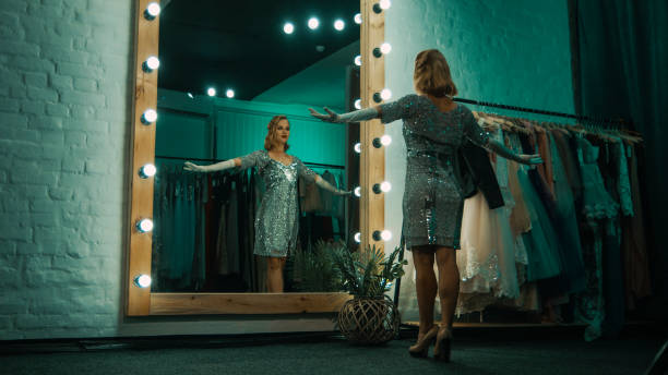 Elegant woman in dressing room before show From below back view of beautiful singer in short sparkling dress and gloves standing in front of mirror practicing show stage actress stock pictures, royalty-free photos & images