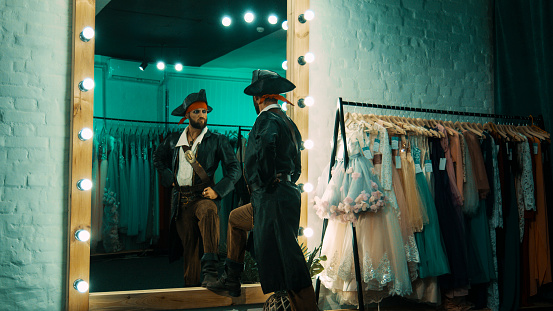 Back view of man wearing costume of pirate and standing in front of mirror in dressing room practicing scene from performance