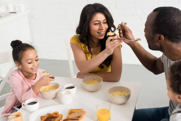 istock wife and husband feeding each other while having breakfast with kids 1007345692