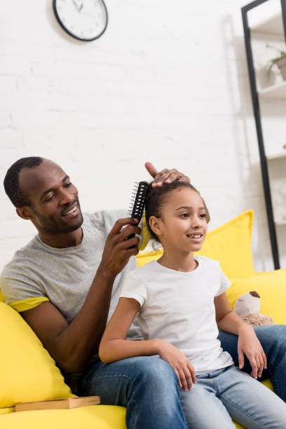 istock father combing hair of daughter while sitting behind her on couch 1007345814