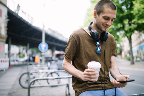 Portrait of young man relaxing outdoors with coffee using mobile phone. Urban man relaxing outside in the city.