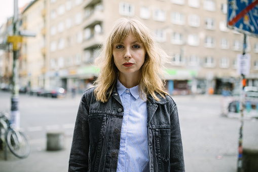 Portrait of young urban woman standing outdoors in the city. Female wearing a jacket looking at camera while standing outside on city street.