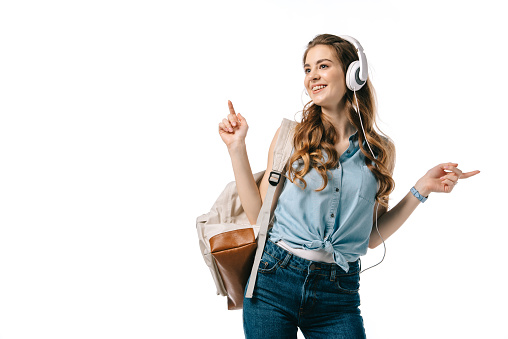 beautiful student listening to music with headphones and dancing isolated on white