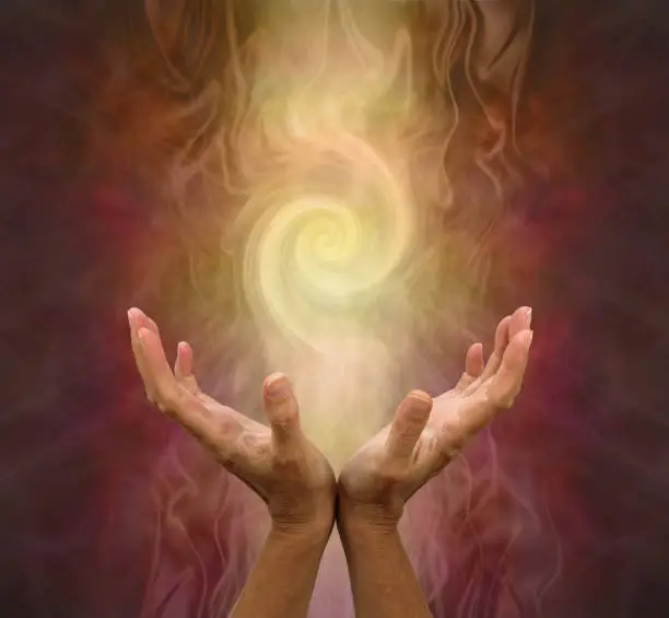 female hands held open and palms upwards with a vortex energy formation above on a warm golden brown background