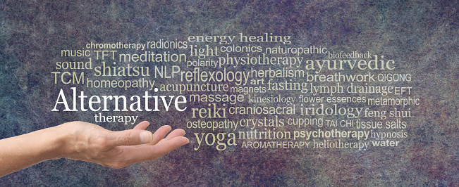 female hand held palm up the words ALTERNATIVE THERAPY in white above surrounded by a relevant word cloud on a rustic dark stone background