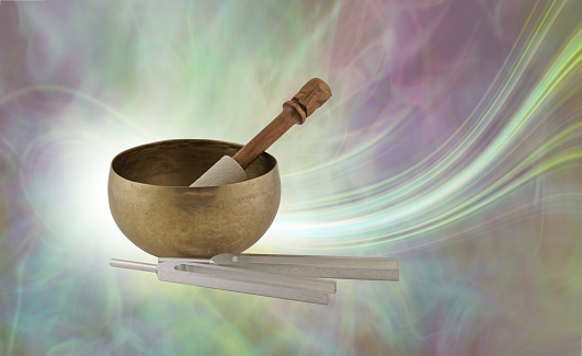 Tibetan Singing Bowl with mallet beside tuning forks against a flowing energy background