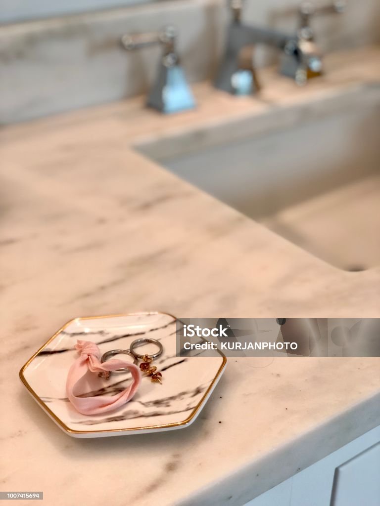Jewelry dish next to sink White jewelry dish with hair band, earrings, and rings next to sink on white marble counters Jewelry Stock Photo