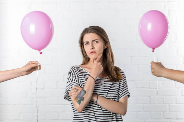 istock Thoughtful girl standing between hands holding pink balloons on white brick wall background 1007425712