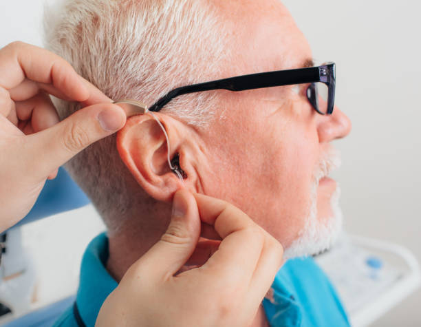 adjusting of a hearing aid for an aged man patient is assisted in setting up the hearing aid. Treatment of hearing of elderly people using a hearing aid. hearing aid photos stock pictures, royalty-free photos & images