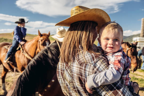 Utah cowgirl mother and baby Portrait of young cowgirl mother and baby  outdoors. Horse in the background.  Outside Salt Lake City, Utah. people laughing hard stock pictures, royalty-free photos & images