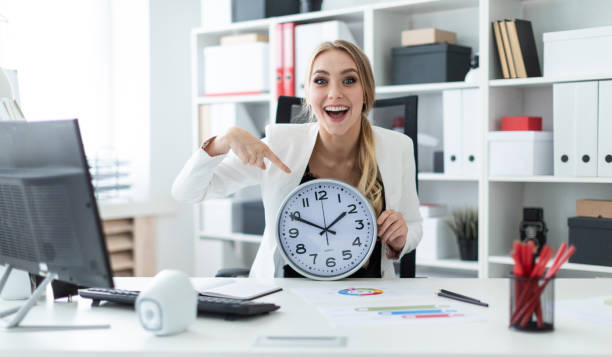 istock A young girl sits at a table in the office and points a finger at the clock face. 1007448342