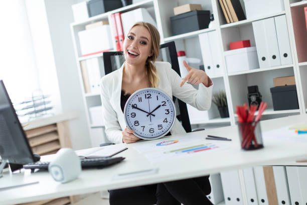 istock A young girl sits at a table in the office and points a finger at the clock face. 1007448352