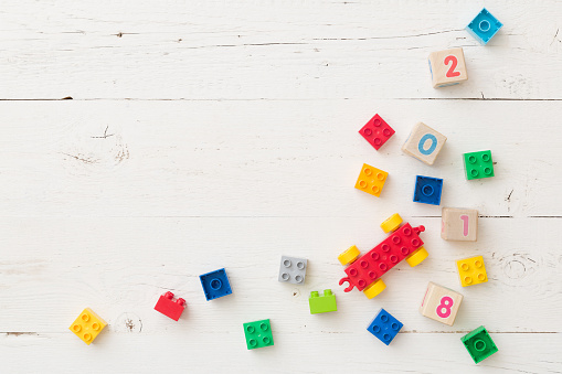 Top view on wooden cubes with numbers and colorful plastic bricks on white wooden table background. School, education and learning concept.