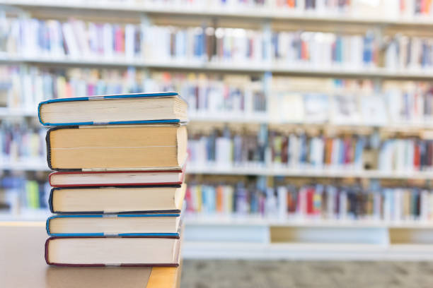 istock Stack of hardcover books against blurry library shelf background 1007461414