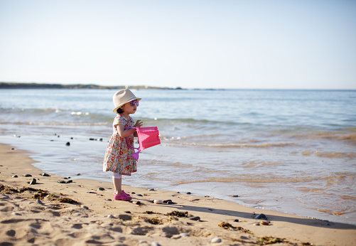 A young girl playing in a puddle with a bucket and spade on a sunny beach in Northumberland.