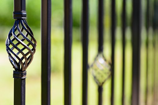 Black decorative metal fence, angular iron rods and curved upper part. Close-up of the decoration, front view.