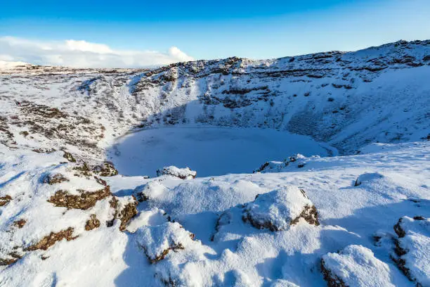 Panoramic view of the Kerid Volcano with snow and ice in the volcanic crater lake in Winter under a clear blue sky. located in the GrÃ­msnes area in south Iceland, along the Golden Circle route.