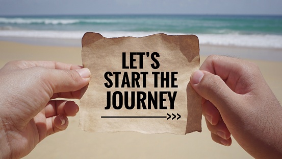 Hands holding a white piece of paper with text ‘Let’s start the journey’ on it. Vintage styled background.