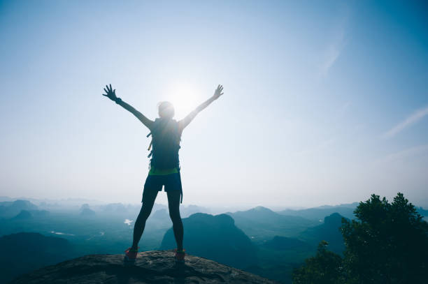 istock Successful female hiker cheering on mountain top cliff edge 1007627526