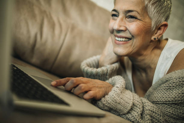 istock Happy mature woman lying on the sofa and using laptop. 1007632874