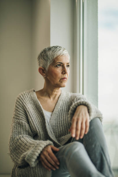 istock Senior woman looking through the window and thinking about something. 1007639760