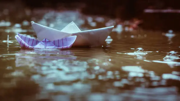 One small and one big paper Boats floating in water puddle during monsoon rains