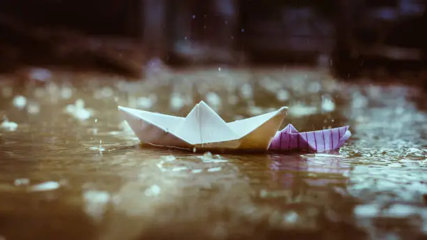 One small and one big paper Boats floating in water puddle during monsoon rains