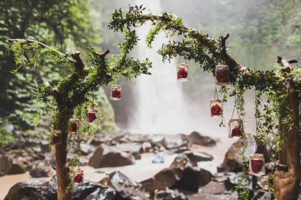 istock Tropical wedding ceremony with waterfall view in jungle canyon. Decorated with green ivy, old branches and hanging lamps 1007645700