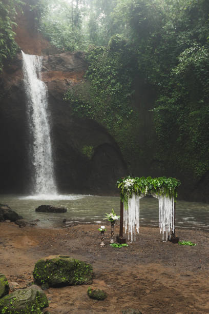 istock Tropical wedding ceremony with waterfall view. White arch decorated with green jungle leaves monstera and fern 1007649314