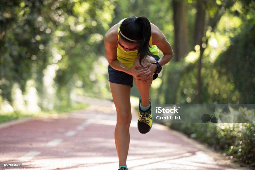 Female runner suffering with pain on sports running knee injury Adult Stock Photo