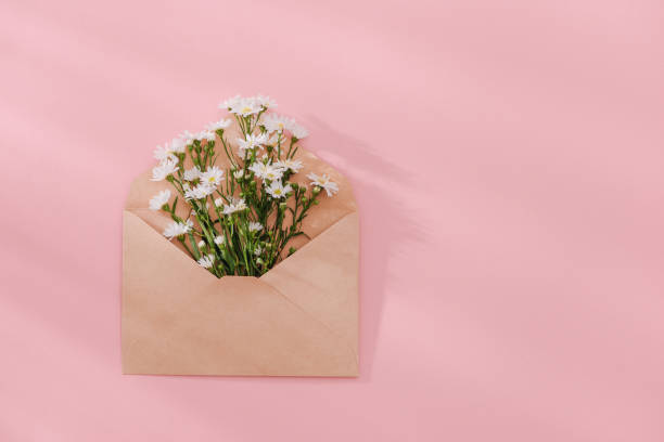istock Opened envelope with flowers arrangements on pink background, top view. Festive greeting concept 1007675246