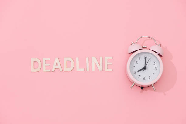istock DEADLINE text with light pink retro alarm clock with shadow on pink background. 1007675360