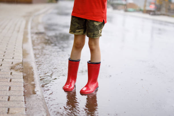 istock Child wearing red rain boots jumping into a puddle. 1007678798