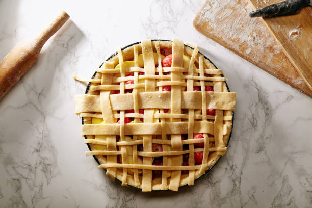 istock Uncooked pie with berries and apples decorated with beautiful piecrust lattice and leaves on white marble table at the kitchen 1007682604