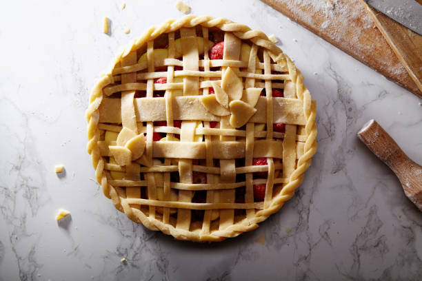 istock Uncooked pie with berries and apples decorated with beautiful piecrust lattice and leaves on white marble table at the kitchen 1007684672