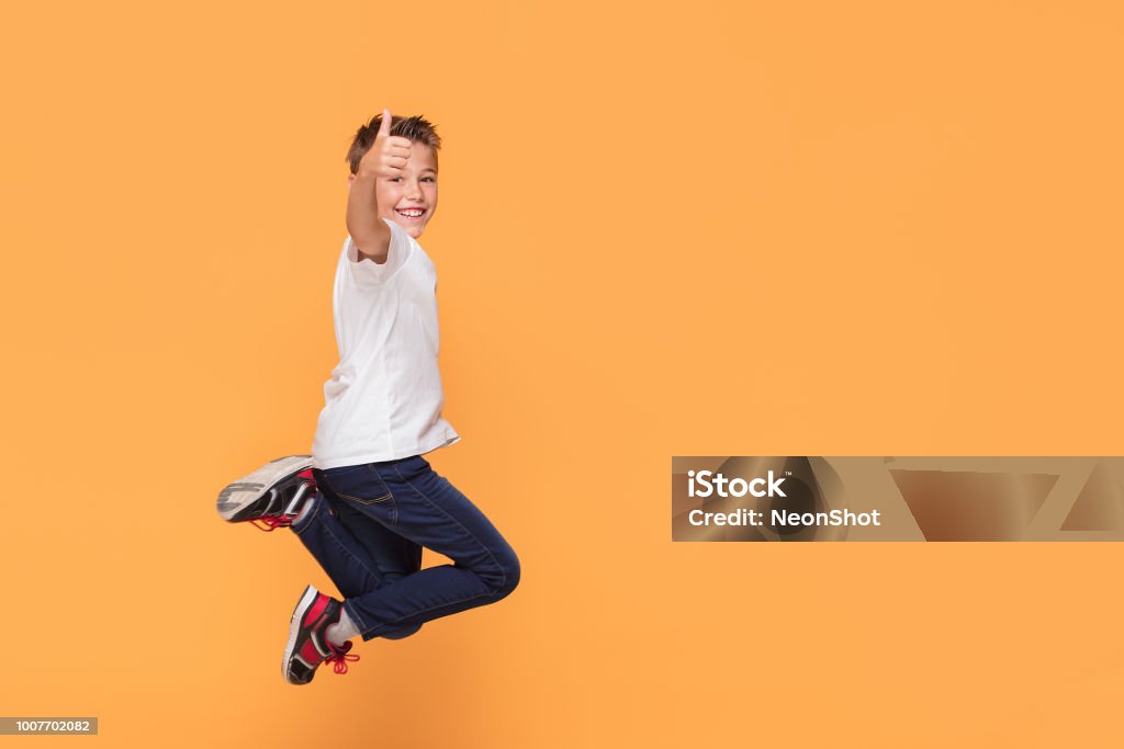 Little boy jumping in the studio, smiling. Little school boy jumping in the studio on a yellow background. Concept of happy childhood. Child Stock Photo