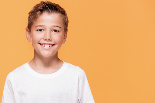 Happy little boy smiling to the camera. A lot of copy space , yellow studio background.