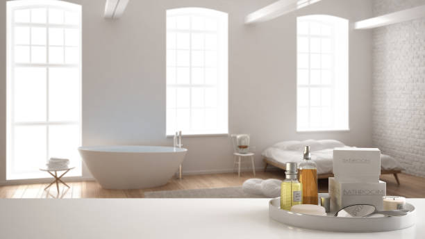 istock Spa, hotel bathroom concept. White table top or shelf with bathing accessories, toiletries, over blurred minimalist bathroom with bedroom, modern architecture interior design 1007706246