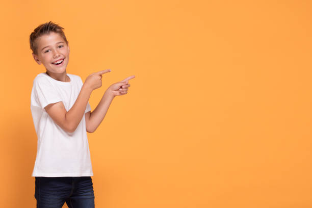 Young emotional little boy on orange studio background.