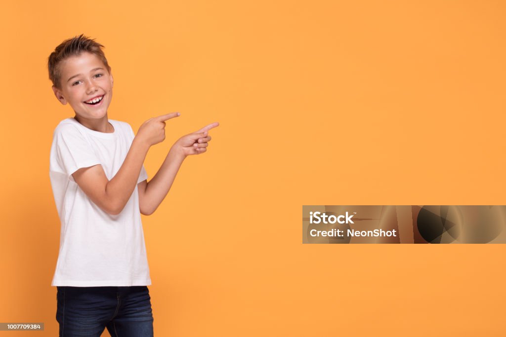 Young emotional little boy on orange studio background. Young emotional handsome boy standing on orange studio background. Human emotions, facial expression concept. Smiling Stock Photo