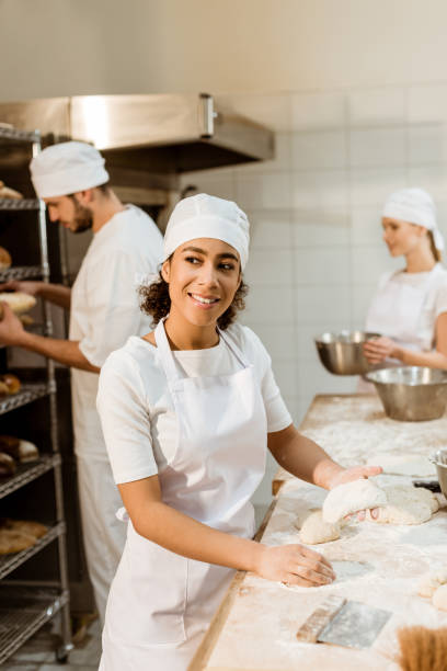 istock happy female baker kneading dough at baking manufacture while her colleagues working blurred on background 1007710162