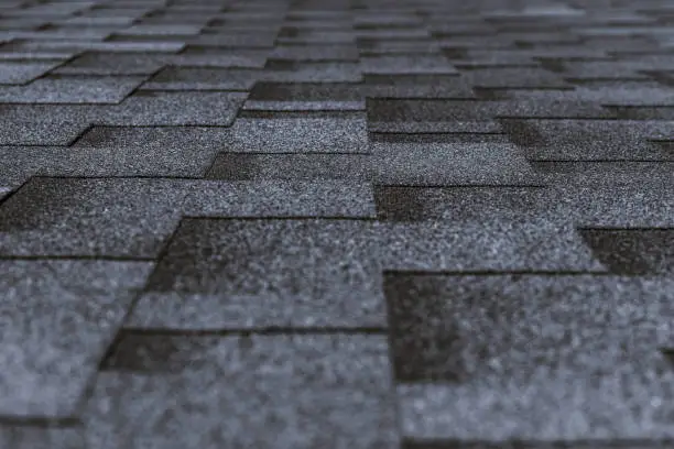 Soft roof tiled gray grainy texture on the top of a village house; grey soft roofing tiles covering a building, focus on the middle distance, shallow depth of field