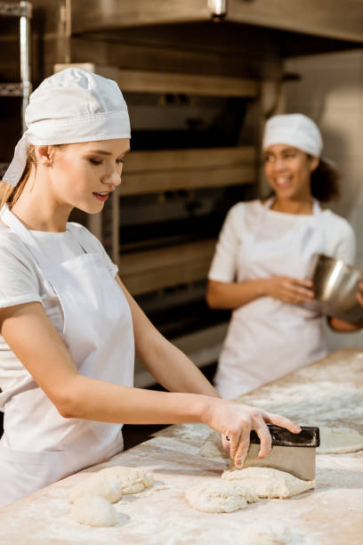 istock young female baker cutting dough with dough knife at baking manufacture while her colleagues working blurred on background 1007716320