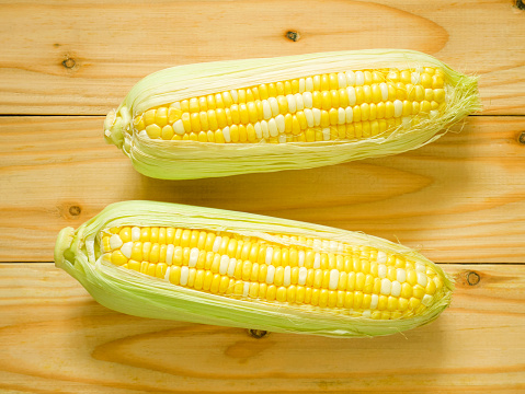 Ears of bicolor sweet corn on rustic wooden background. Top view.