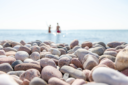 Two kids taking a fresh summer Baltic sea bath in the bright sunlight on a stony island beach at Gotska Sandön with pebbles shaped by the ocean in the foreground