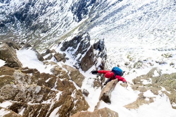 A climber ascending a snow covered ridge Climber ascending a snow covered Striding Edge ridge below Helvellyn in the Lake District UK. striding edge stock pictures, royalty-free photos & images