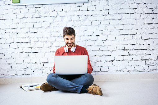 Male student sitting on floor with notebook and laptop studying. Portrait of startup entrepreneur at work