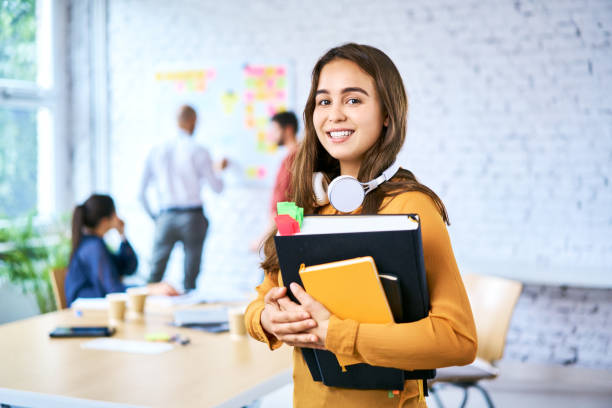 Portrait of female student holding books in classroom. Young woman looking at camera and smiling stock photo