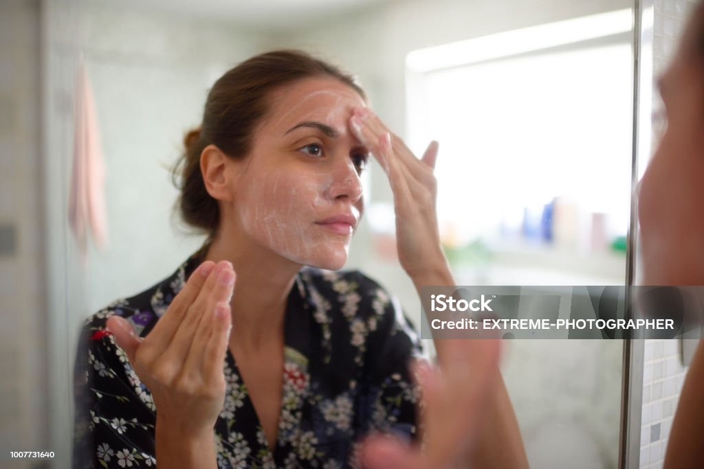 Woman in the bathroom Young female in the bathroom looking in the mirror and taking care of her facial skin. One Woman Only Stock Photo