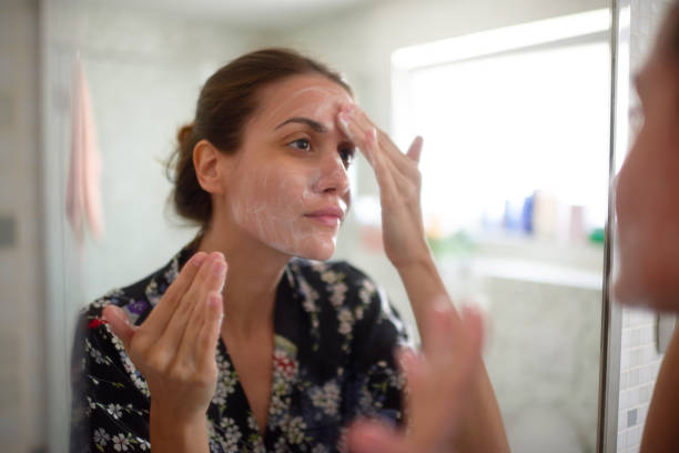 Woman in the bathroom Young female in the bathroom looking in the mirror and taking care of her facial skin. face cream stock pictures, royalty-free photos & images